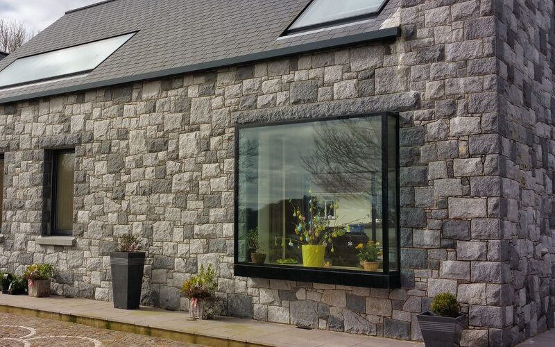 a frameless box window into a grey stone cottage in Guernsey