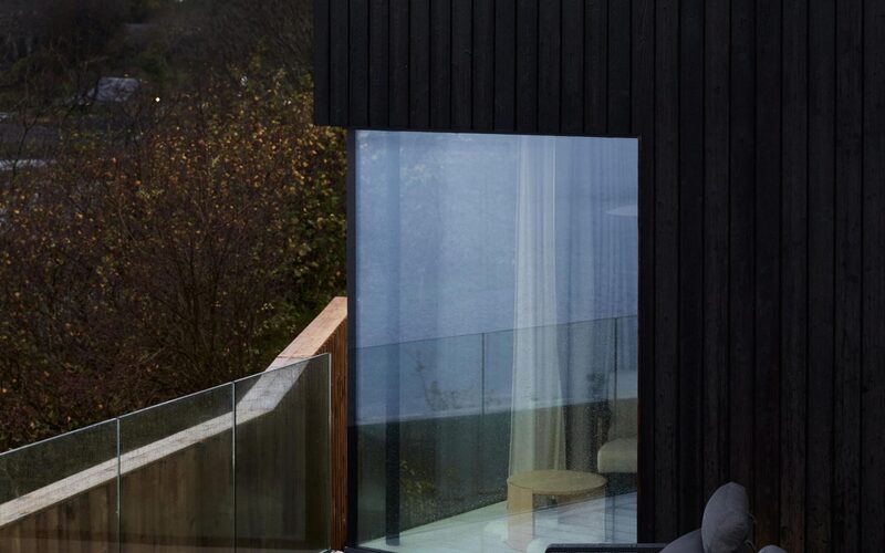 a frameless glass corner window set into black timber overlooking a lake