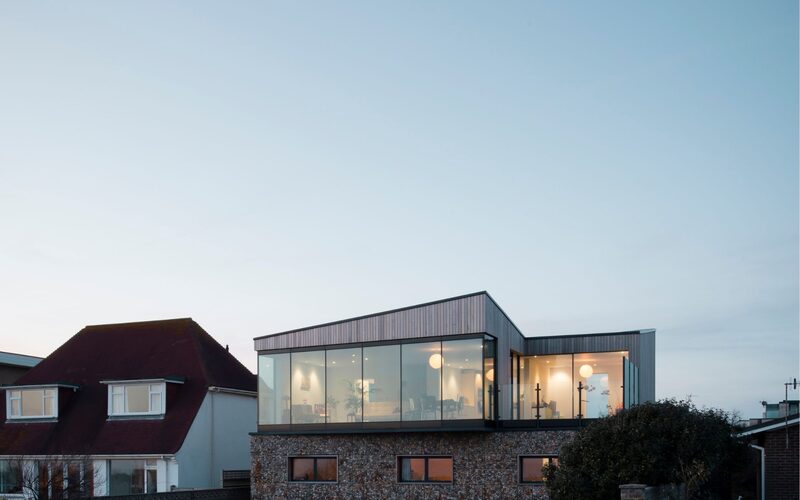 a glass walled beach house right on the beach in old fort road shown at dusk